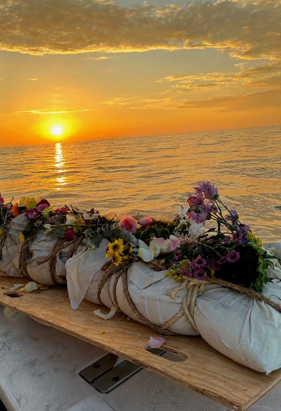 A shrouded committal, dressed with flowers on the vessel's board, against a Pacific sunset.
